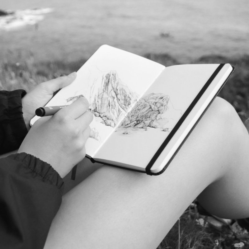 A person sitting outside drawing in a sketchbook