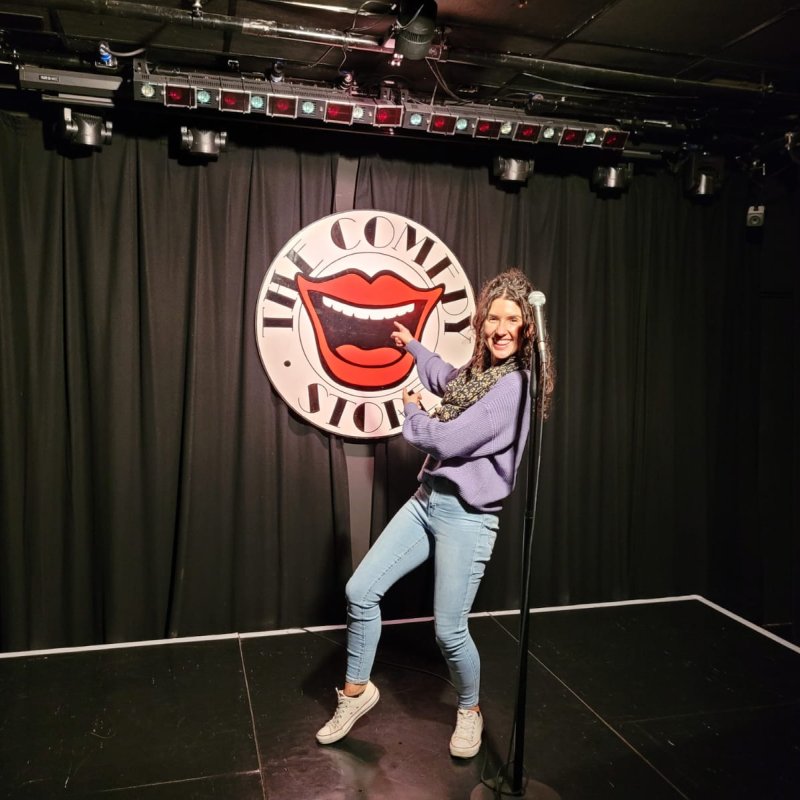 Comedy writing student Kayleigh Jones stood on a stage in front of The Comedy Store sign 