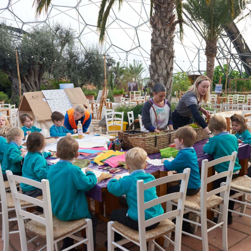 A group of primary school children seated at a table with adults helping them do crafts