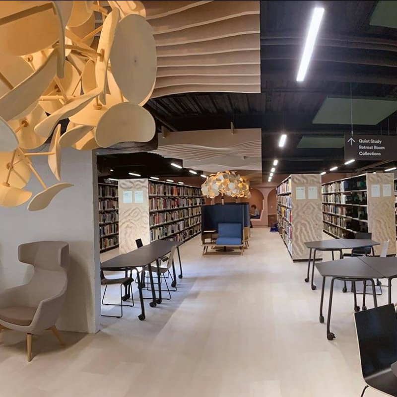 A view of Falmouth University campus library with lights, chairs and rows of bookshelves