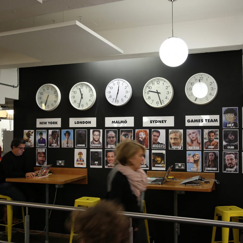 People sat at high desks with clocks and names of cities on a black wall