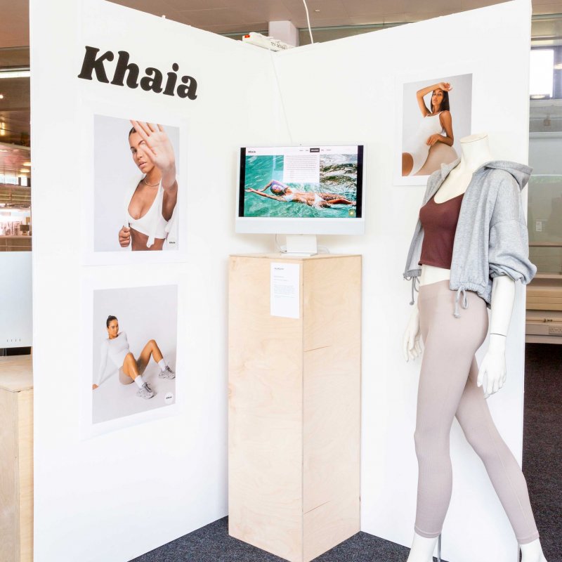 A marketing booth for sportswear brand 'Khaia' - a mannequin models leggings, crop top and hoodie, with images of the brand set against a white wall