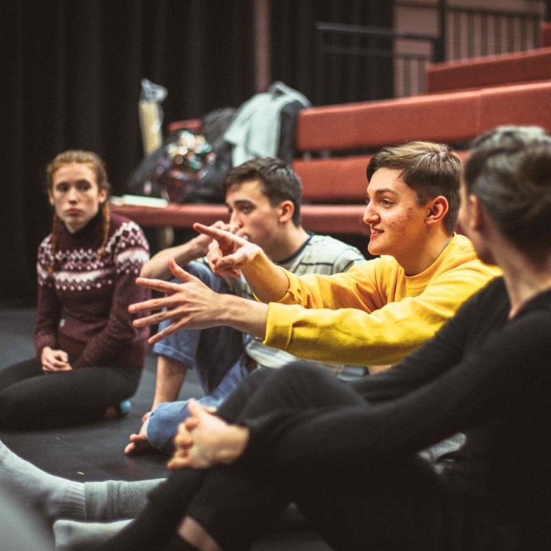 Group of students sat in performance space discussing acting