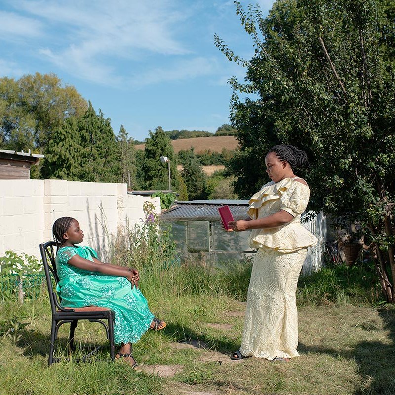 A mother standing taking a photo on a phone of her daughter in a chair