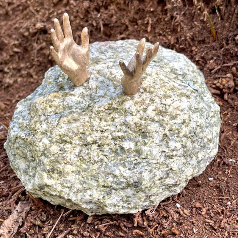 Photo of miniature sculpture - a piece of granite rock with tiny bronze hands sticking out of the top