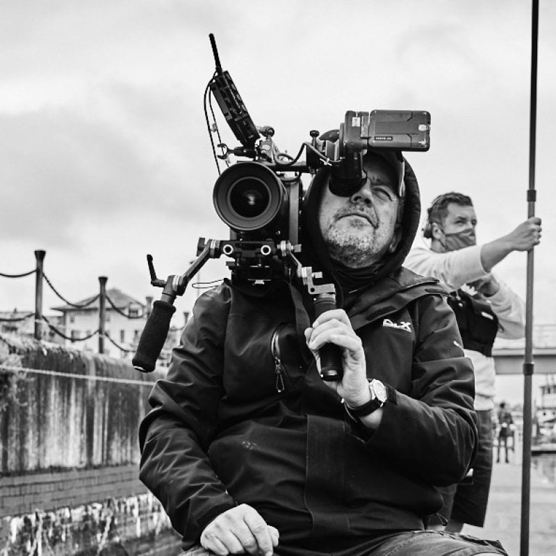 A man looks through a film camera on the set of London Kills 