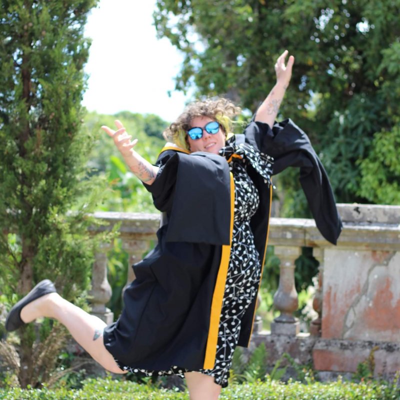 A woman wearing a graduation gown leaps into the air