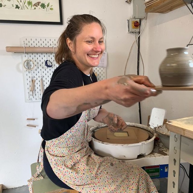 A woman smiles as she shapes an object from clay