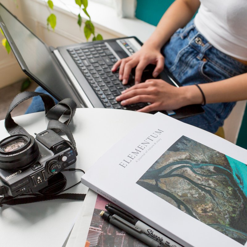 A desk with a stack of books, acamera and a laptop