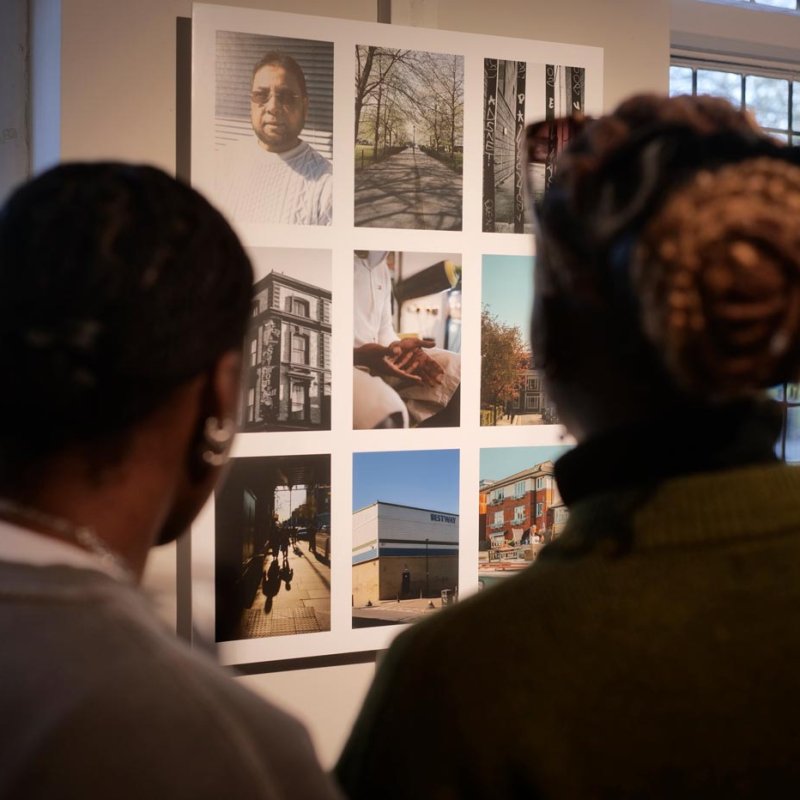 Two people looking at photographs displayed on a wall at Oxford House