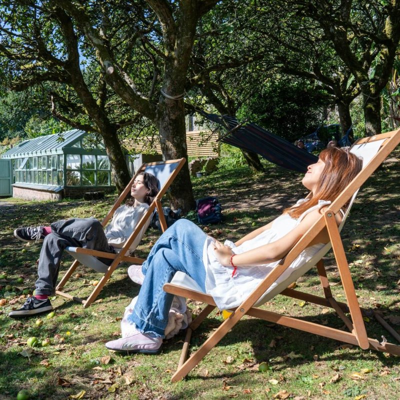 Two Falmouth University students in deckchairs in the orchard of Penryn Campus