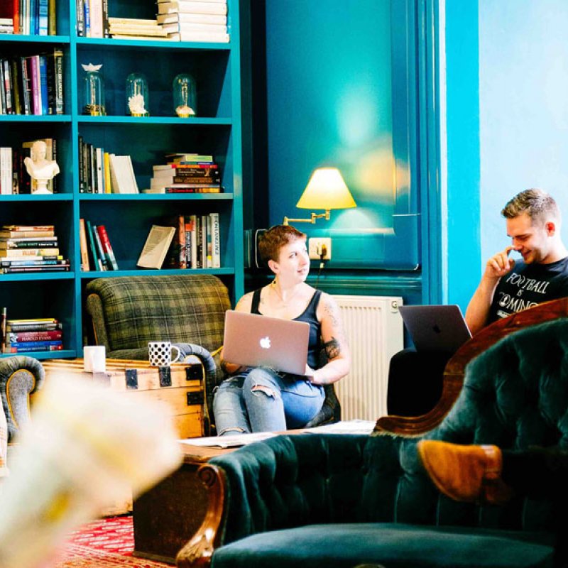 Falmouth University students sat on sofas in a blue room with bookshelves