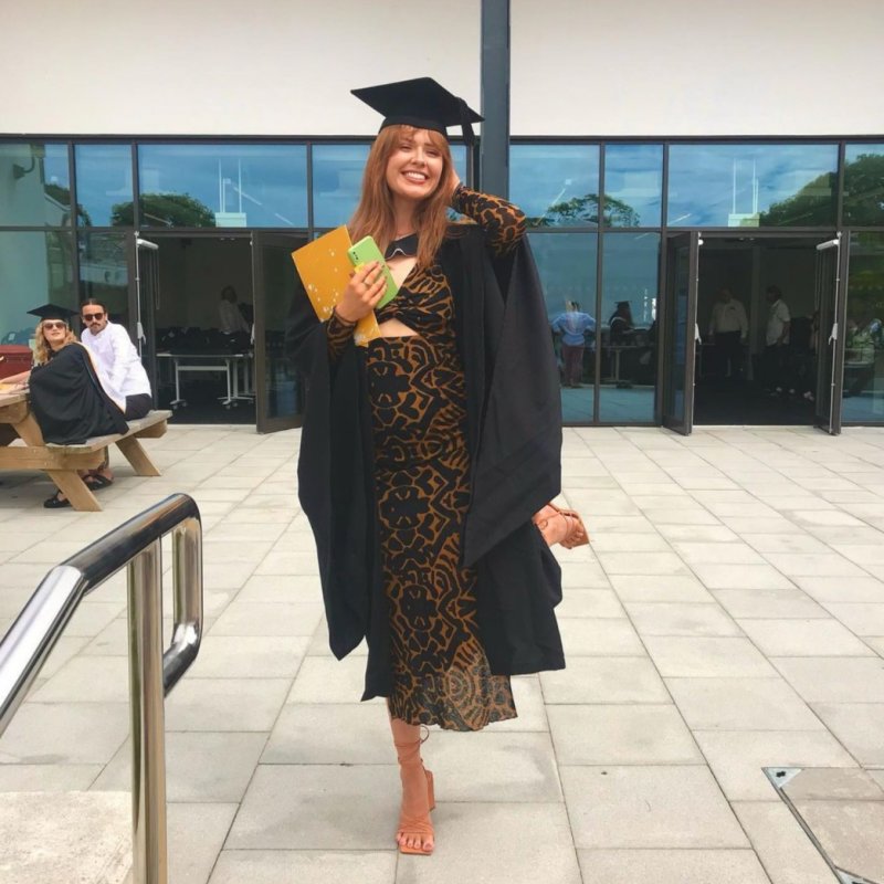 A woman poses in a graduation gown