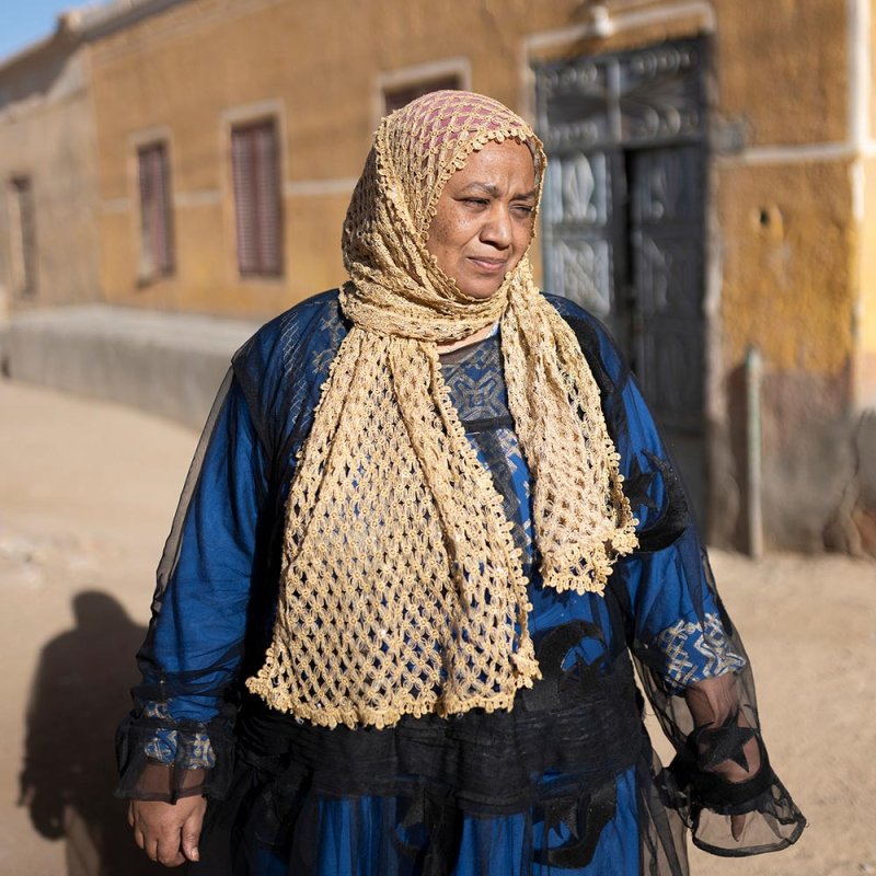 Photograph of a woman in a blue dress and headscarf, standing in the street