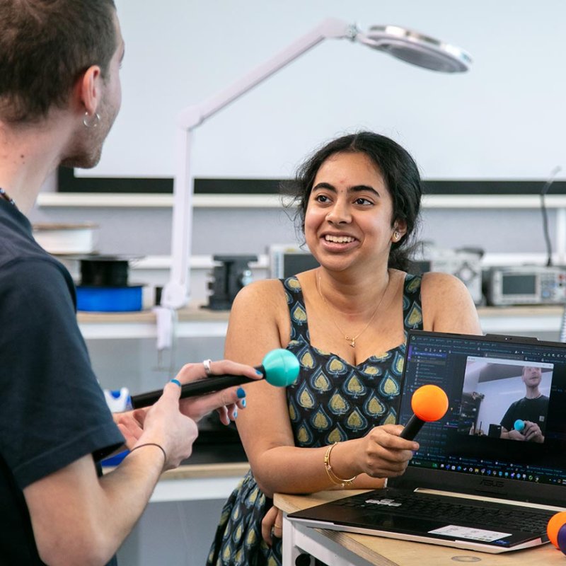 A male and female Robotics student holding hardware next to a laptop