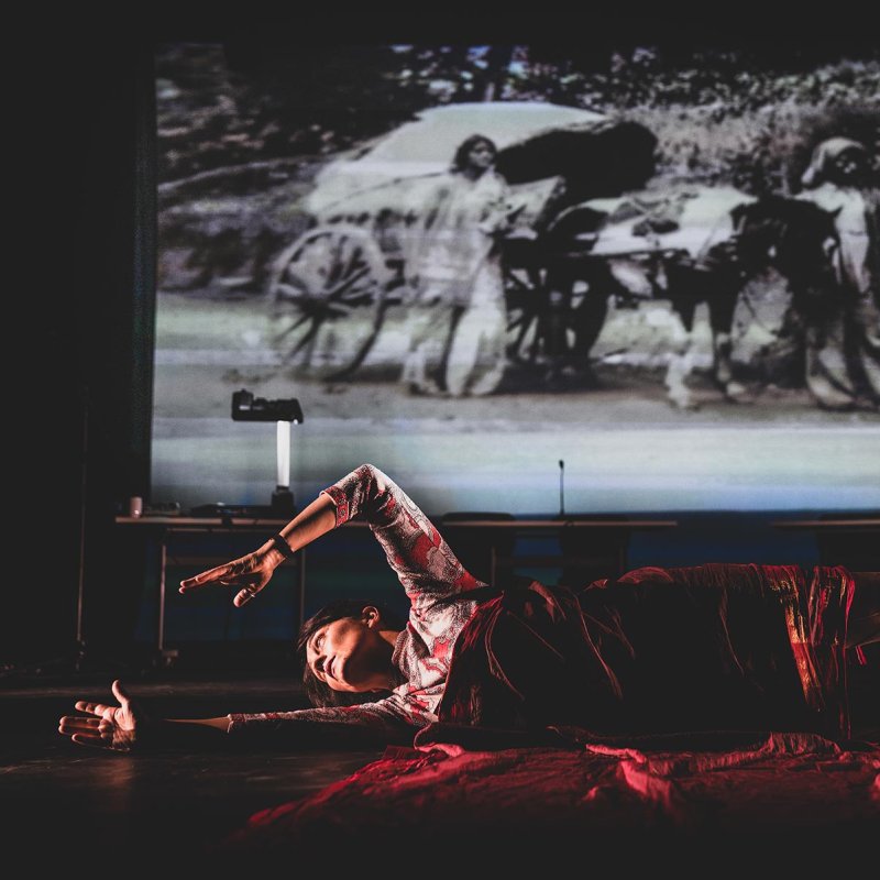 A woman wrapping herself in red fabric while lying on a stage