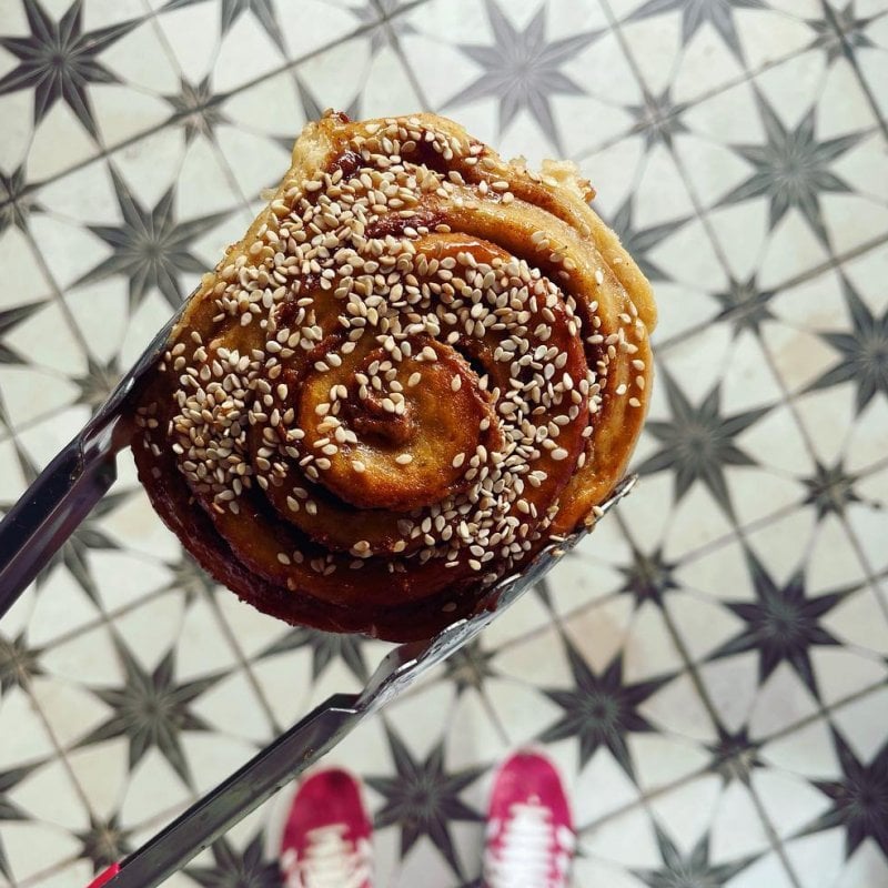 Metal tongs holding a cinnamon roll above a tiled floor