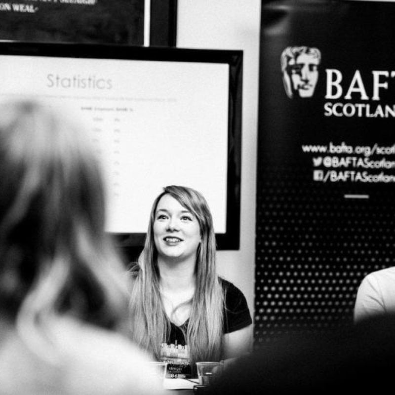 A woman sat giving a talk in front of a BAFTA film poster