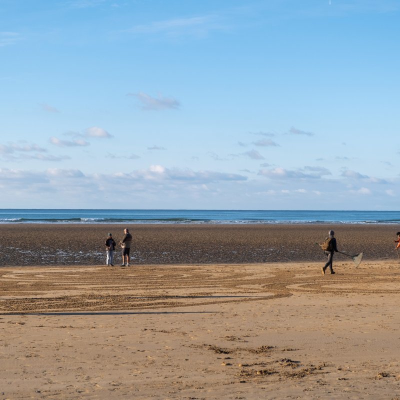 Landscape photo of Falmouth University students working on sand art project on Cornish beach.