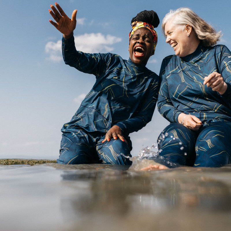 Two women having fun by the sea wearing Finisterre full coverage Seasuit