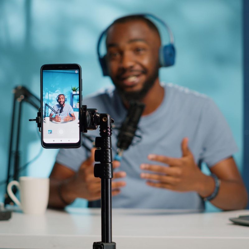 A man wearing headphones filming himself with his phone on a tripod
