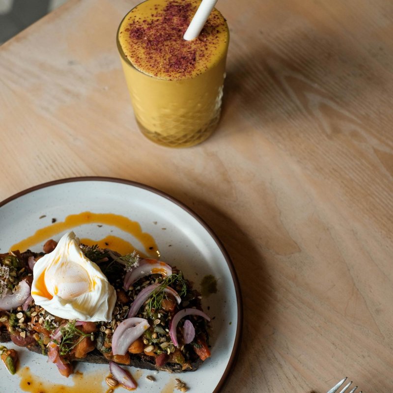 A wooden table with a glass of orange juice and a plate with a poached egg