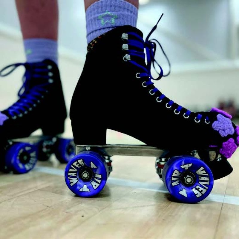Close up of legs wearing black roller skates with blue wheels and purple flowers on the toe