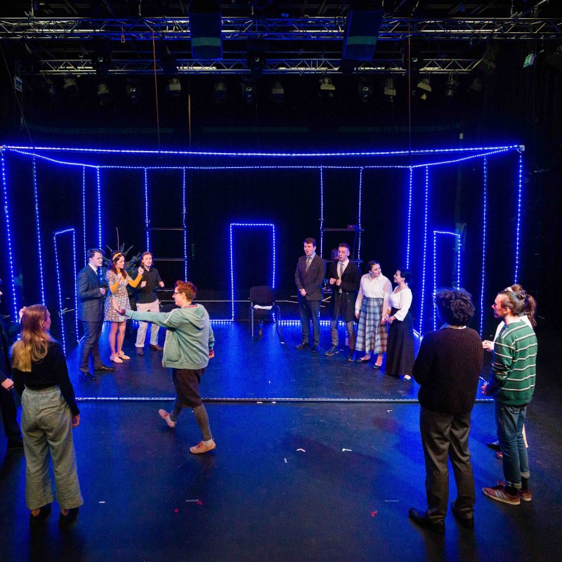 A group of acting students on a stage lit with blue lights