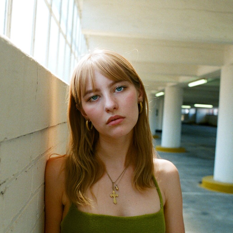 Photo of a woman leaning against the wall of an underground car park, looking into the camera.