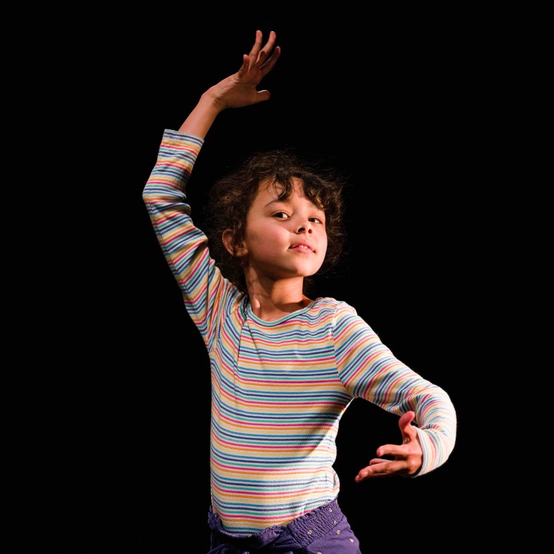 Child strikes dance pose with one arm above their head