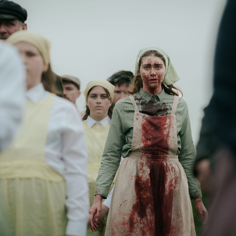 A woman dressed in 19th century fashion covered in blood