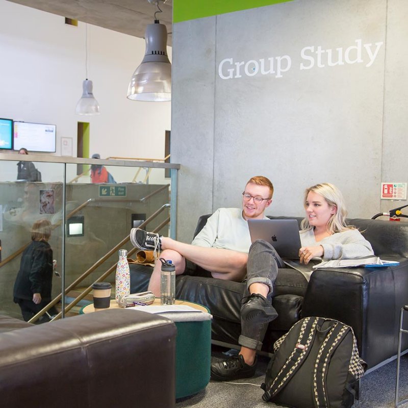 Two students sitting on a brown leather sofa with glass barrier