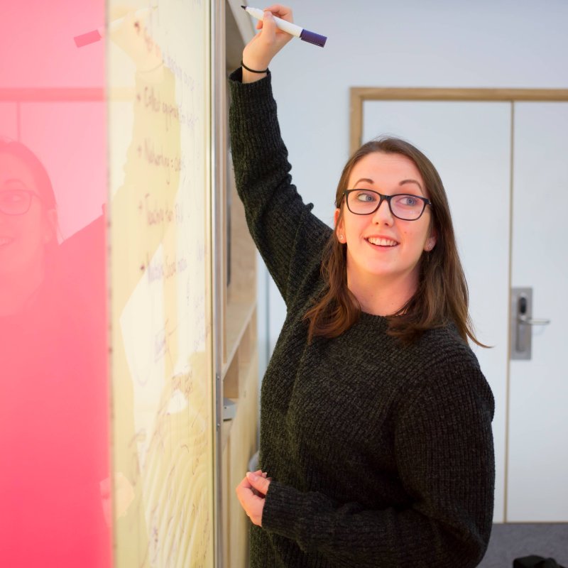 Student writing on a vibrant pink and yellow wall board, Falmouth University