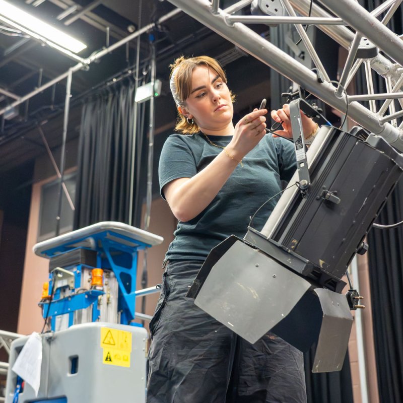 A Technical Theatre Arts student rigging a light