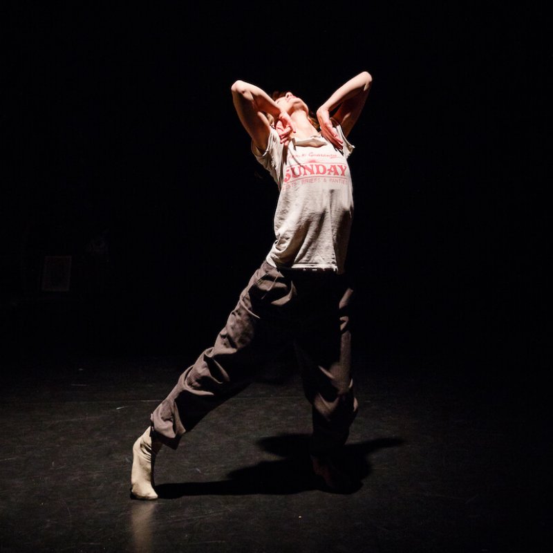 Dancer with leg stretched out stretching to the sky with arms folded in at the elbows.