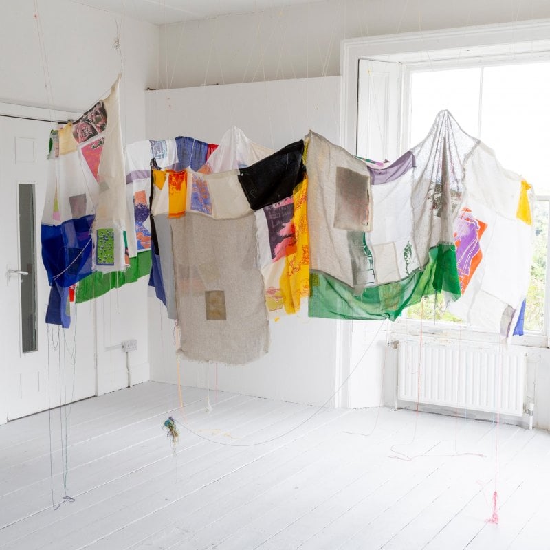 Colourful cloth is hung in a brightly lit white room