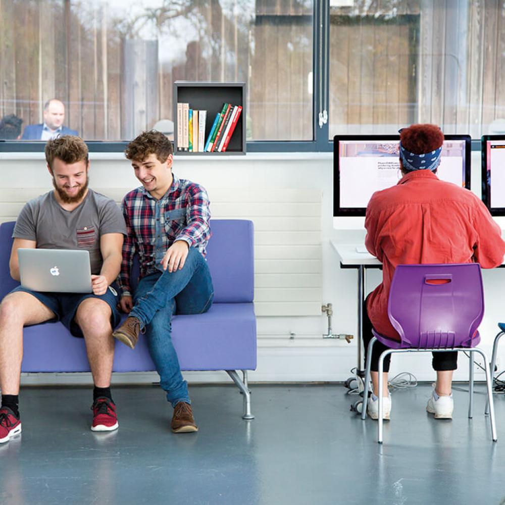 Three business management students working at a laptop and desktop