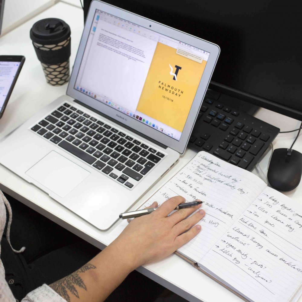 A Journalism student working at a laptop and holding a phone