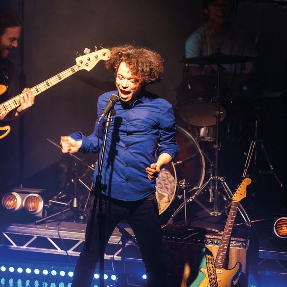 Student singing and jumping on stage in front of guitarist