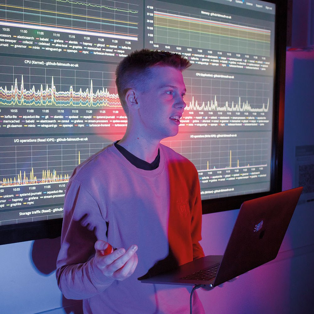 Student stood in front of large screen with code and graphs on