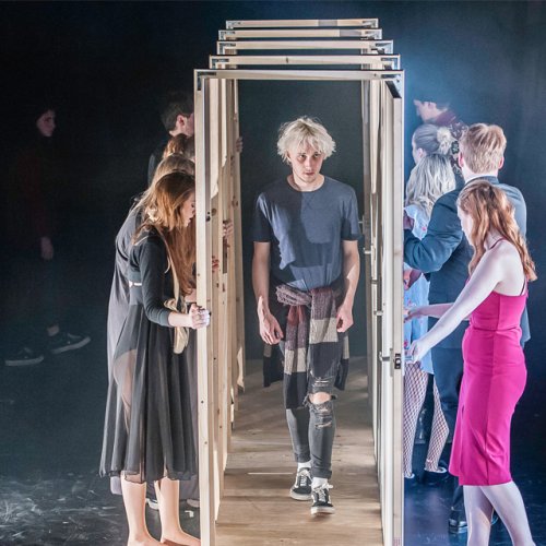 Actor walking through a series of open doors held by other members of the cast.
