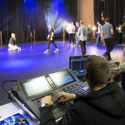 Group of students on mixing desk and on stage setting up with microphones.