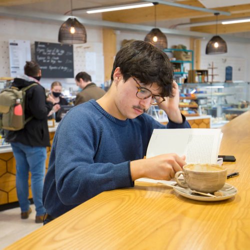 A student reading at a table in the cafe on Penryn Campus