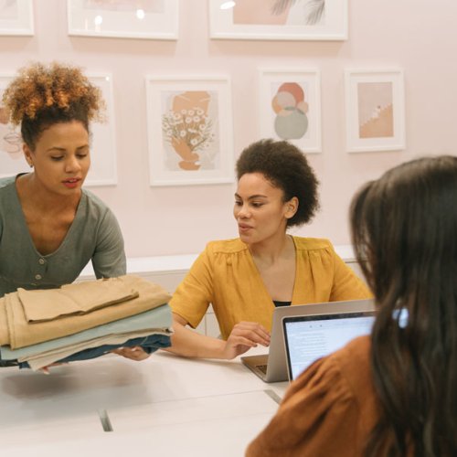 Three Sustainable Fashion students looking at fabric