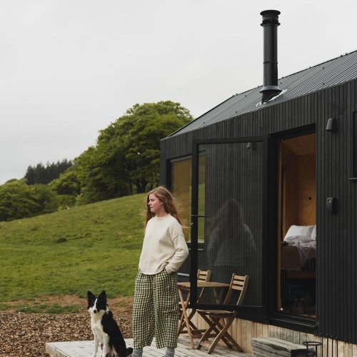 A young woman and a collie outside a cabin