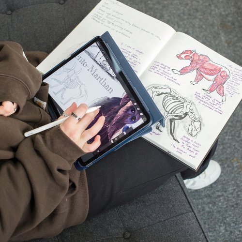 Close up of student sketching on a tablet over hand drawn paper sketches