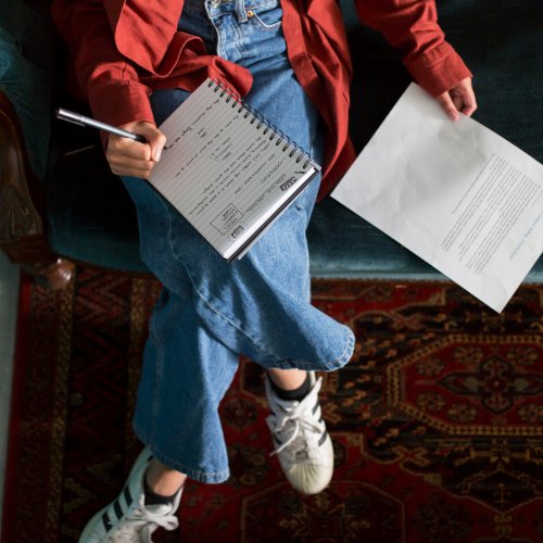 An aerial photo of a girl sat on a sofa with a notebook on her lap and a piece of paper next to her