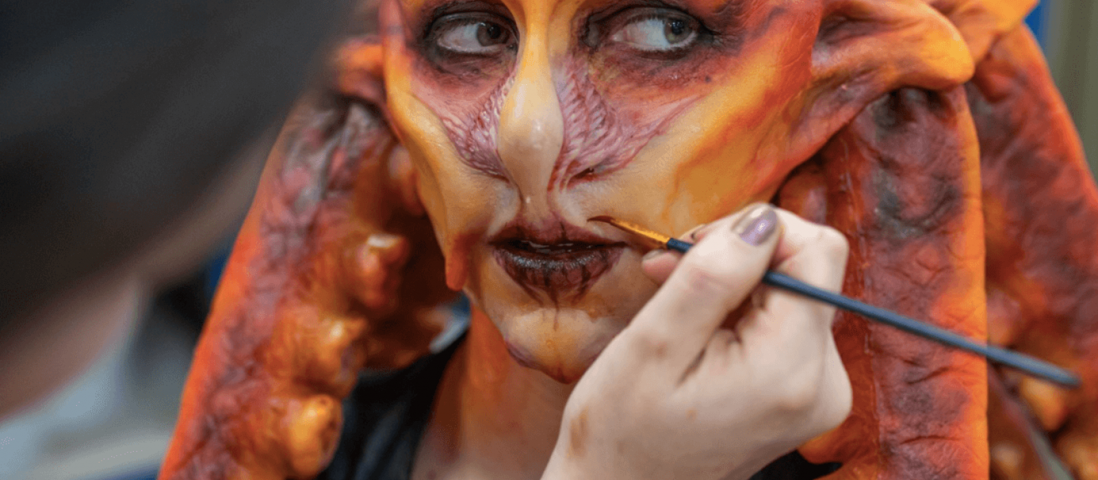 A person wearing a prosthetics orange mask with a hand and a paintbrush