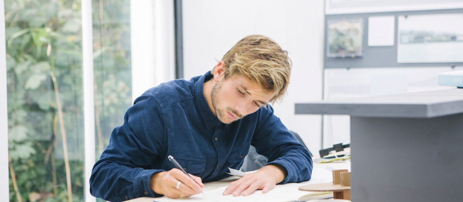 Falmouth University Architecture student working at a desk, wearing a blue shirt