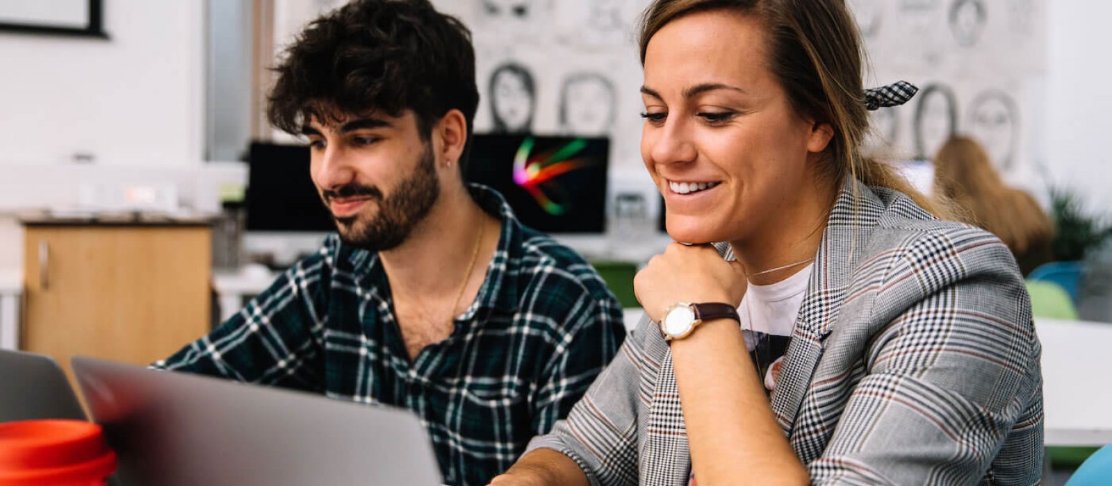 Two Falmouth University Creative Advertising students smiling at a laptop